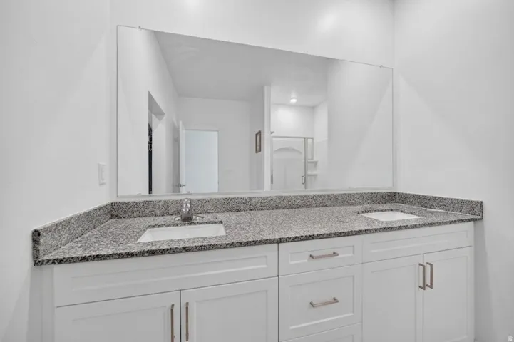 Double vanity with integrated sinks, granite-style countertop, white shaker-style cabinetry, and brushed nickel hardware