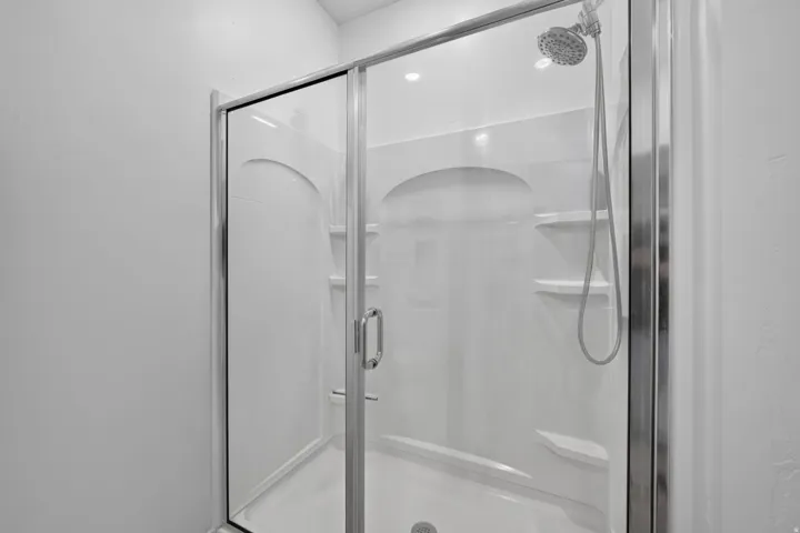 Enclosed shower with clear glass door, chrome hardware, and built-in shelving