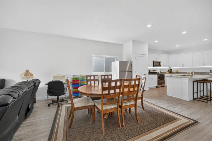 Expansive open-concept living space with wood-finish flooring, recessed lighting, and a kitchen featuring white cabinetry and stainless steel appliances