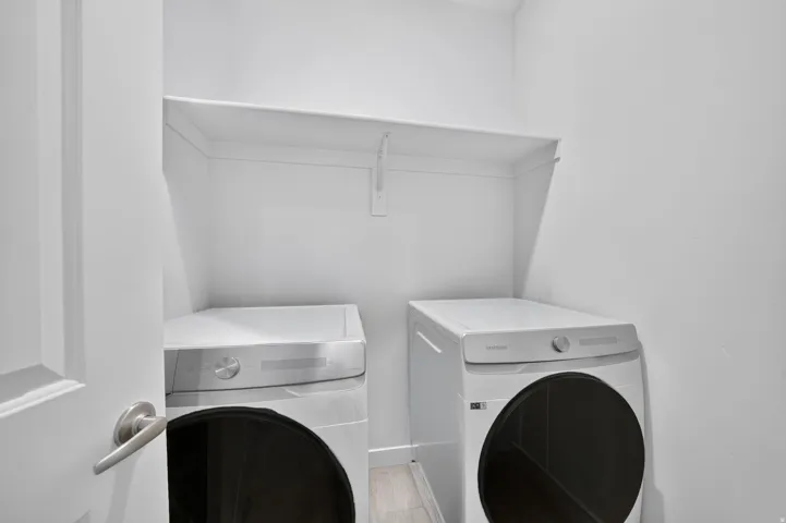 Dedicated laundry area featuring a built-in shelf, light-toned wood-finish flooring, and a contemporary door with brushed nickel hardware