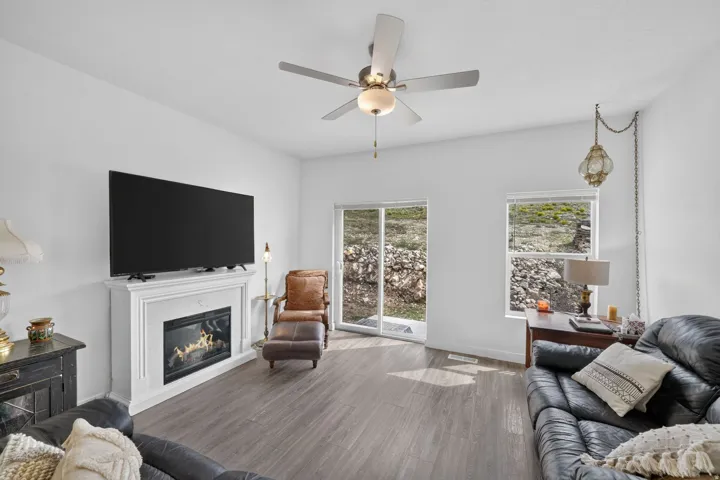 Living area with wood-finish flooring, a white mantel fireplace, and a ceiling fan with integrated lighting
