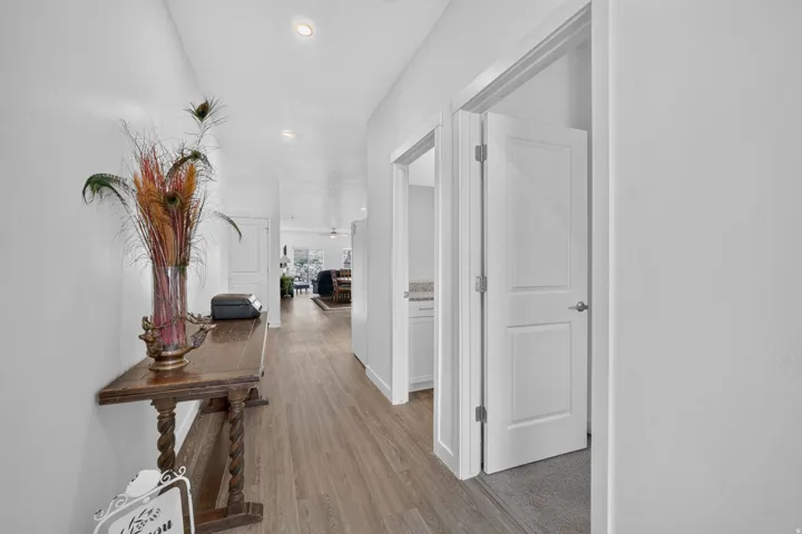 Recessed lighting illuminates wood-finish flooring throughout this corridor, featuring white walls and white interior doors