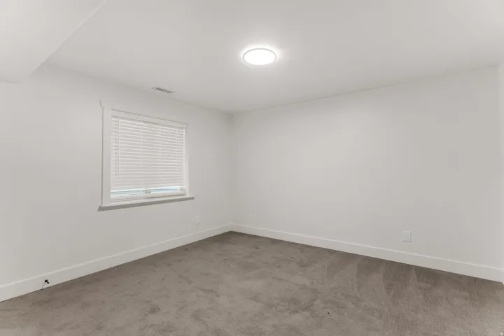 Neutral wall finishes with a window featuring blinds, complemented by recessed lighting and grey carpeting