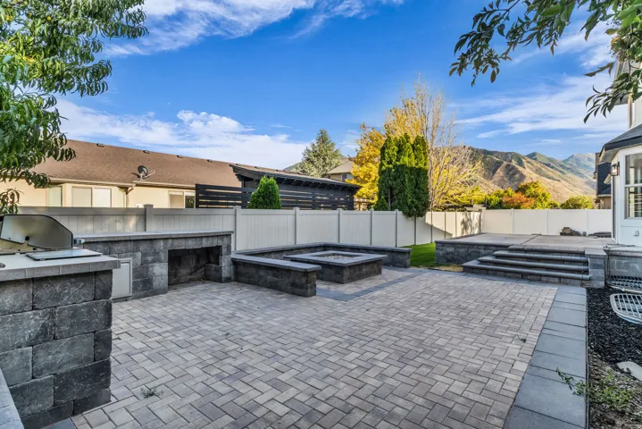 Paved patio area featuring an outdoor kitchen, built-in fire pit, and tiered hardscaping