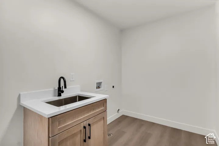 Light wood-finish cabinetry with black hardware, stainless steel sink, black gooseneck faucet, white countertop, and wood-finish flooring