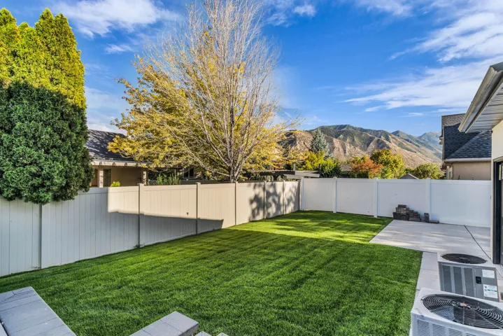 Expansive backyard featuring a manicured lawn, concrete patio, and white privacy fencing