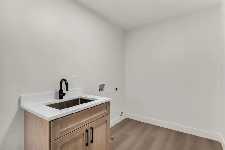 Light wood-finish cabinetry with black hardware, stainless steel sink, black gooseneck faucet, white countertop, and wood-finish flooring
