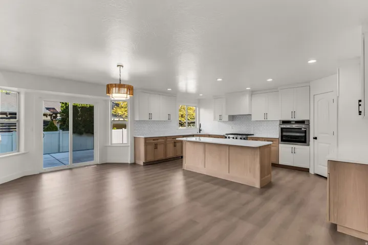 Open-concept living space with wood-finish flooring, a contemporary kitchen island, white cabinetry, integrated stainless steel appliances, and sliding glass patio doors
