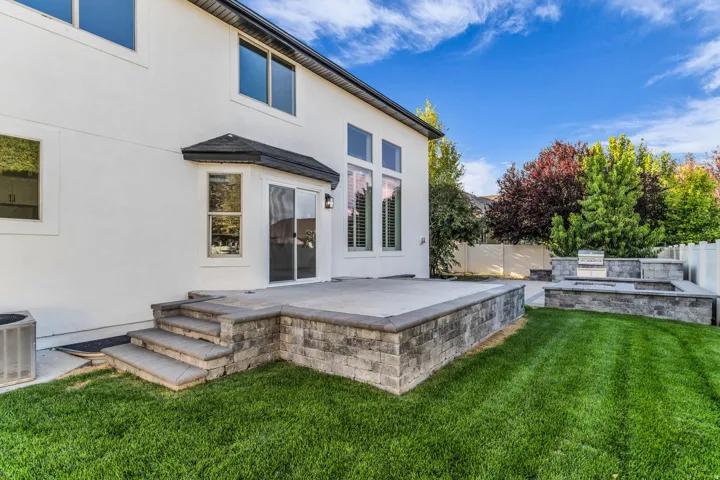 White stucco exterior with multiple windows, a sliding glass door, an outdoor patio, a built-in grill, and a stone-clad fire pit