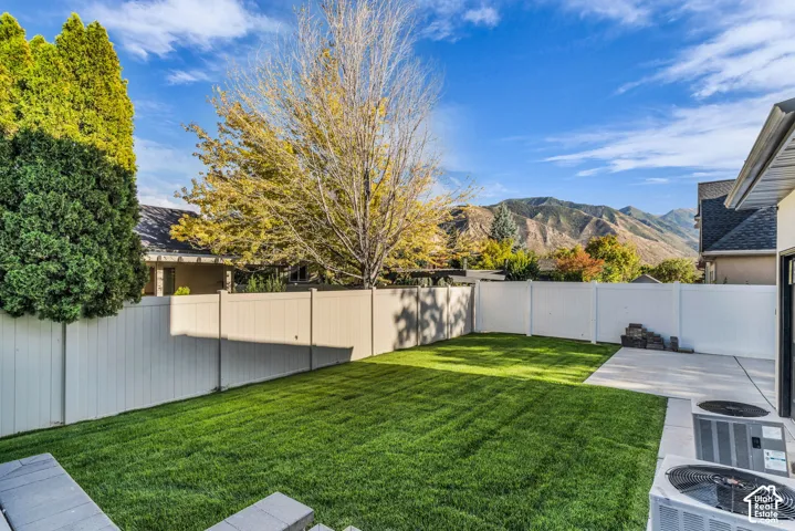 Expansive backyard featuring a manicured lawn, concrete patio, and white privacy fencing