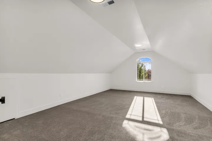 Vaulted ceiling with recessed lighting, arched window, built-in storage access, and wall-to-wall carpeting
