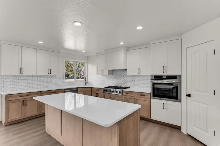 Kitchen featuring a center island with a light-toned wood finish, white countertops, two-tone cabinetry, a subway tile backsplash, and stainless steel appliances
