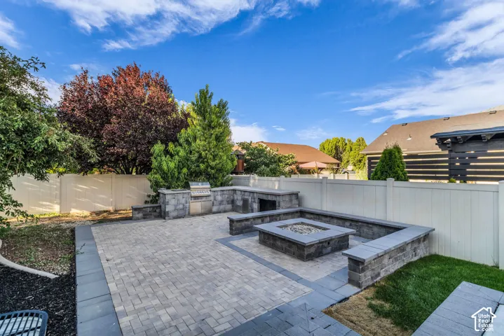 Expansive paver patio with a built-in outdoor kitchen, integrated fire pit, and surrounding stone seating