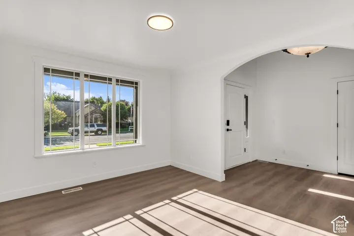 Wood-finish flooring, white walls, arched entryway, window with grilles, and a flush-mount ceiling light
