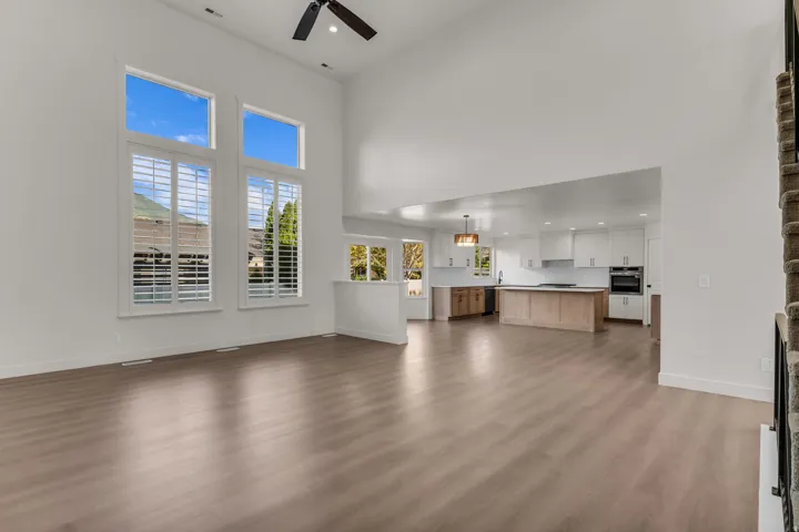 Vaulted ceilings, wood-finish flooring, tall windows with plantation shutters, open-concept kitchen with white cabinetry, and a central island with wood-finish base