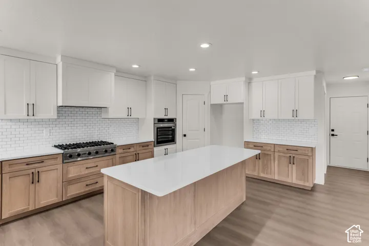 White and wood-finish cabinetry with matte black hardware, white subway tile backsplash, white countertops, and a kitchen island