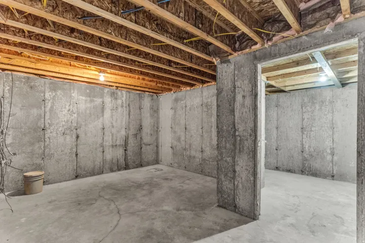 Unfinished concrete basement with exposed wood joists and concrete walls