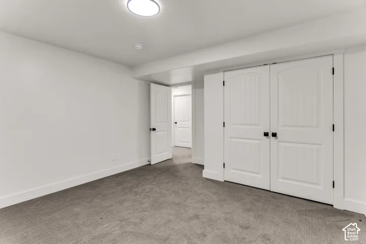 Recessed ceiling lighting, white walls, gray carpet flooring, white paneled doors with black hardware, and integrated ceiling beam