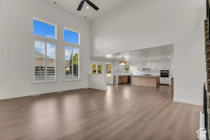 Vaulted ceilings, wood-finish flooring, tall windows with plantation shutters, open-concept kitchen with white cabinetry, and a central island with wood-finish base