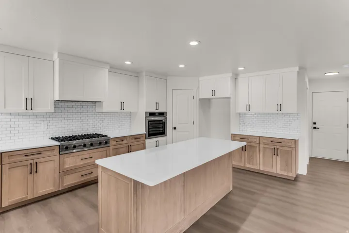 White and wood-finish cabinetry with matte black hardware, white subway tile backsplash, white countertops, and a kitchen island