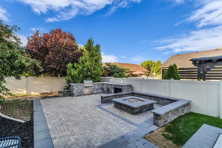 Expansive paver patio with a built-in outdoor kitchen, integrated fire pit, and surrounding stone seating