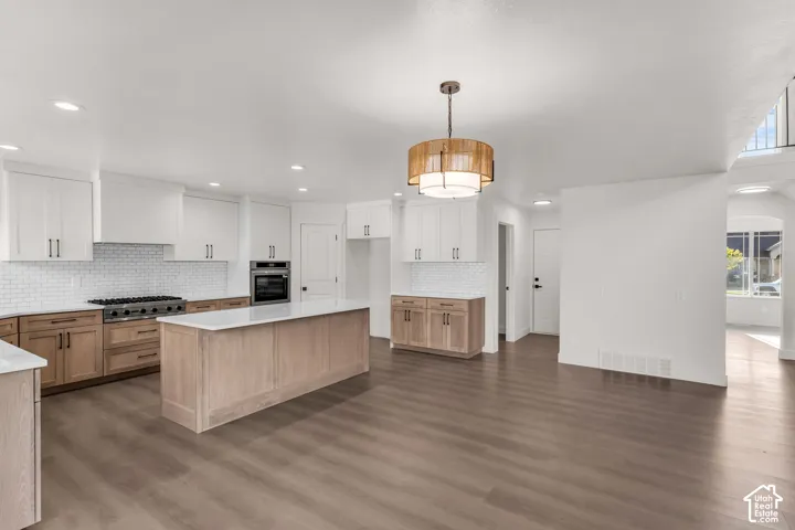 Modern kitchen with a large center island, white subway tile backsplash, stainless steel appliances, and wood-finish flooring