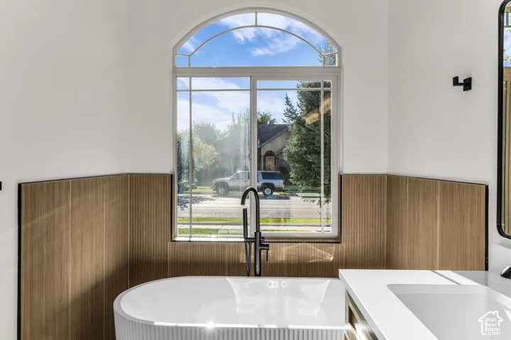 Arched window with gridded panes, contemporary freestanding tub with ribbed detailing, matte black tub filler, white countertop with integrated sink, and wood-finish accent paneling