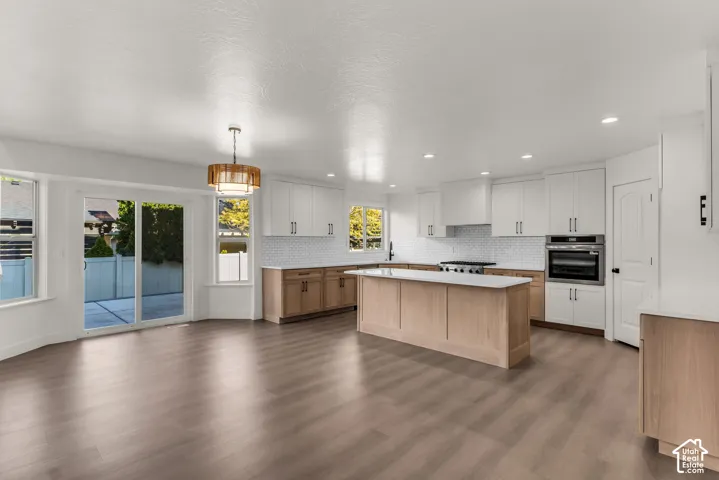 Open-concept living space with wood-finish flooring, a contemporary kitchen island, white cabinetry, integrated stainless steel appliances, and sliding glass patio doors