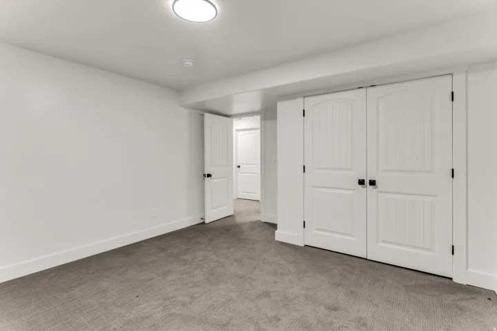 Recessed ceiling lighting, white walls, gray carpet flooring, white paneled doors with black hardware, and integrated ceiling beam
