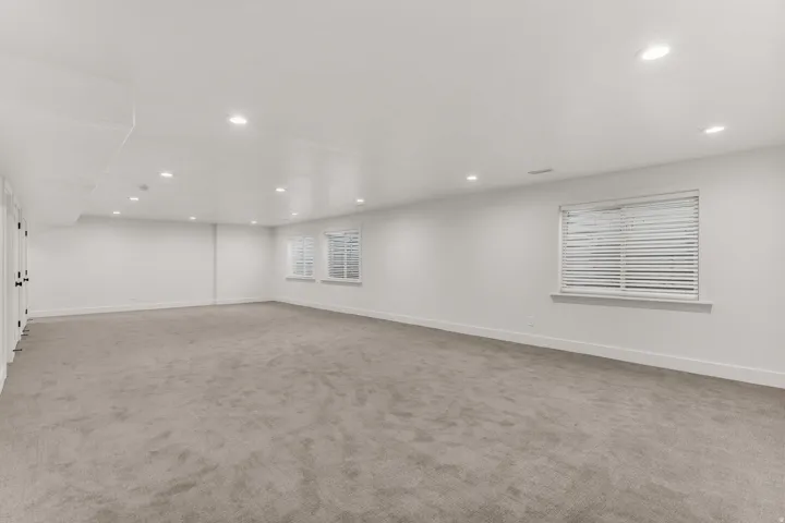 Spacious room featuring neutral carpeting, recessed lighting, white walls, and multiple windows with blinds
