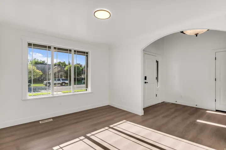 Wood-finish flooring, white walls, arched entryway, window with grilles, and a flush-mount ceiling light
