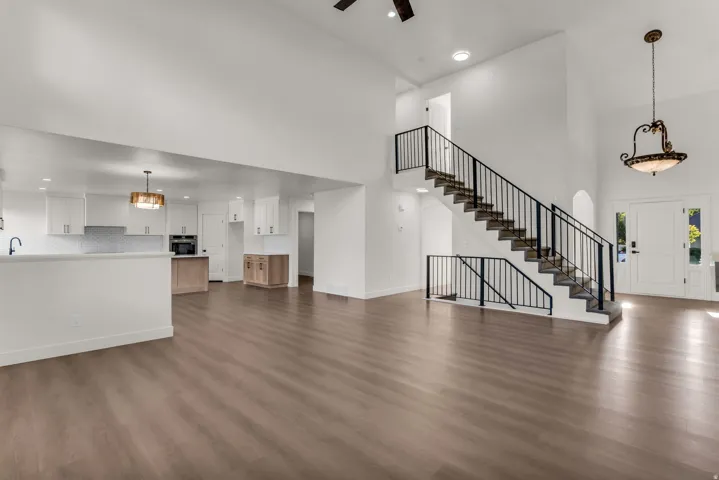 Vaulted ceilings, wood-finish flooring, staircase with black metal railings, white cabinetry, and a patterned tile backsplash