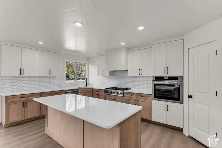 Kitchen featuring a center island with a light-toned wood finish, white countertops, two-tone cabinetry, a subway tile backsplash, and stainless steel appliances
