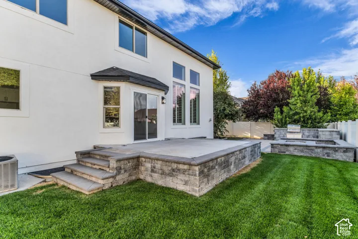 White stucco exterior with multiple windows, a sliding glass door, an outdoor patio, a built-in grill, and a stone-clad fire pit