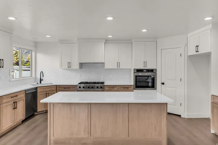 Kitchen featuring a central island with white countertop, wood-finish base cabinetry, stainless steel appliances, and white subway tile backsplash
