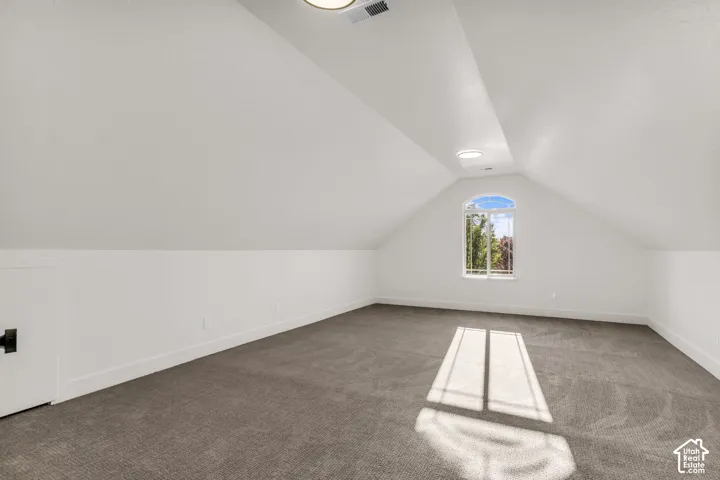 Vaulted ceiling with recessed lighting, arched window, built-in storage access, and wall-to-wall carpeting