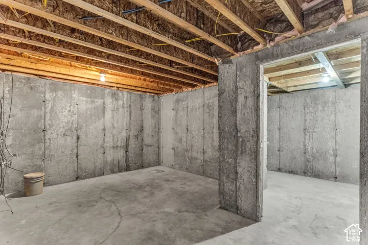 Unfinished concrete basement with exposed wood joists and concrete walls