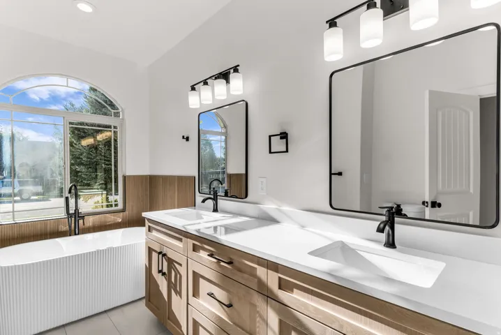 Bathroom featuring a freestanding tub, arched window, dual vanity with solid surface countertops, and matte black fixtures