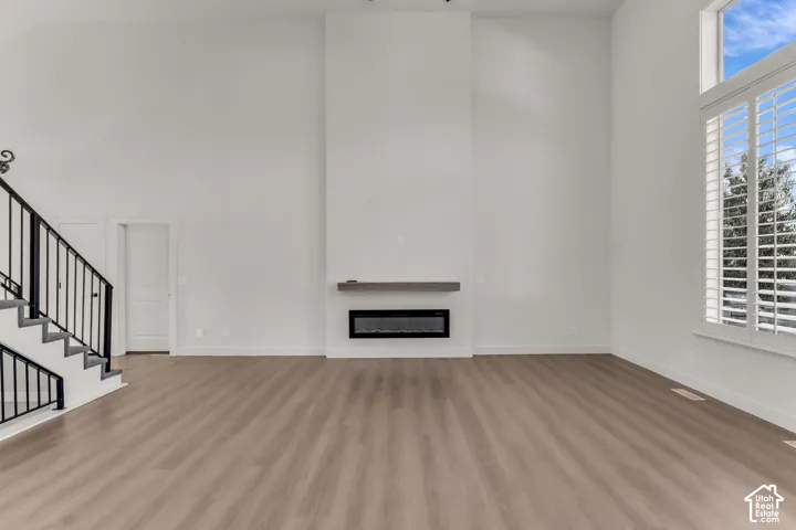 Wood-finish flooring, high ceilings, linear electric fireplace with wood-finish mantel, plantation shutters, and a staircase with a black wrought iron railing