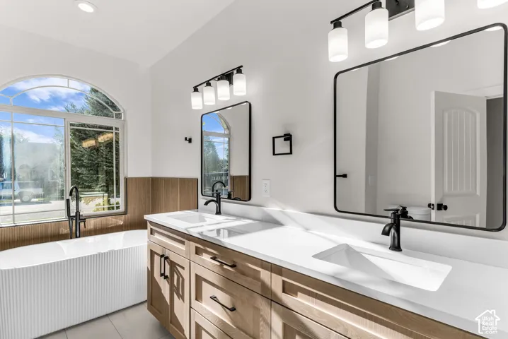 Bathroom featuring a freestanding tub, arched window, dual vanity with solid surface countertops, and matte black fixtures