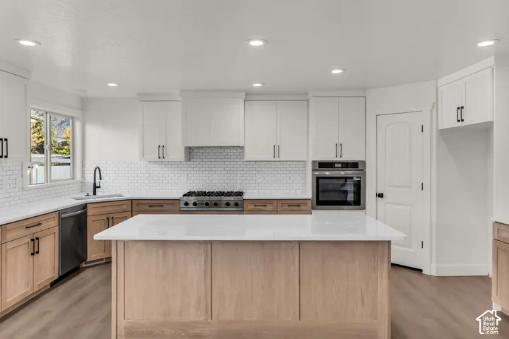 Kitchen featuring a central island with white countertop, wood-finish base cabinetry, stainless steel appliances, and white subway tile backsplash