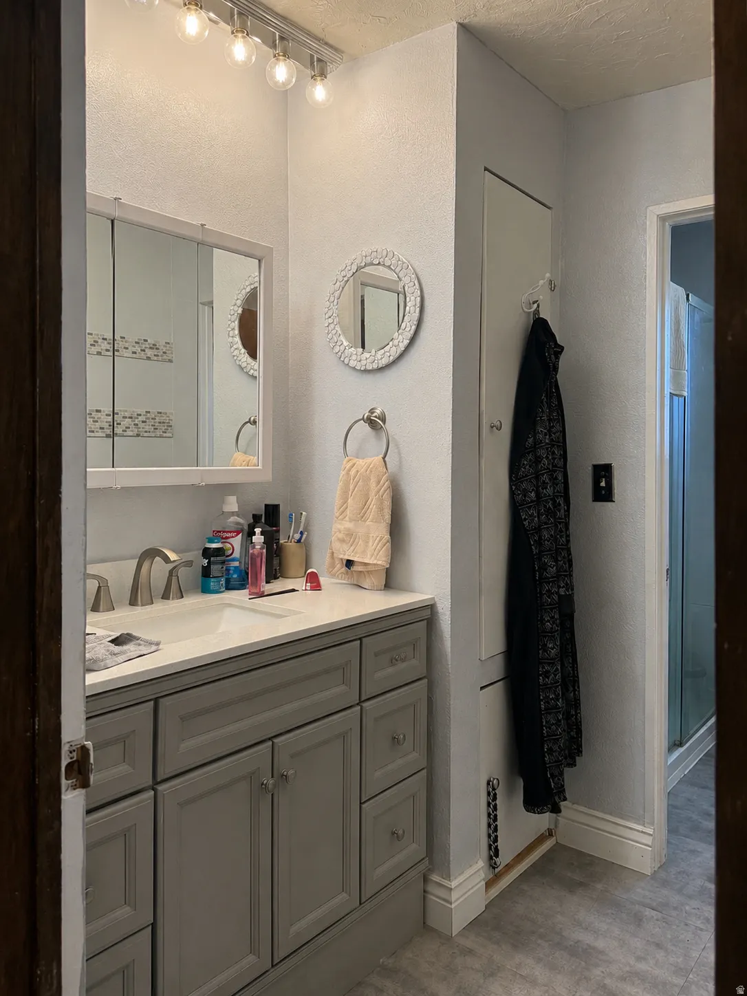 Vanity with integrated sink, modern wall-mounted light fixture, built-in storage cabinet, and tile flooring