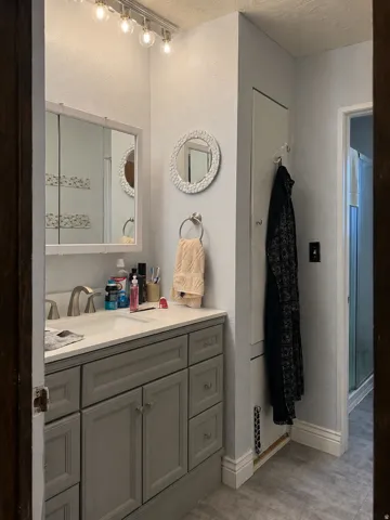 Vanity with integrated sink, modern wall-mounted light fixture, built-in storage cabinet, and tile flooring