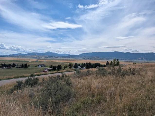 Expansive land parcel with natural vegetation, featuring distant mountain ranges and a scattered rural community