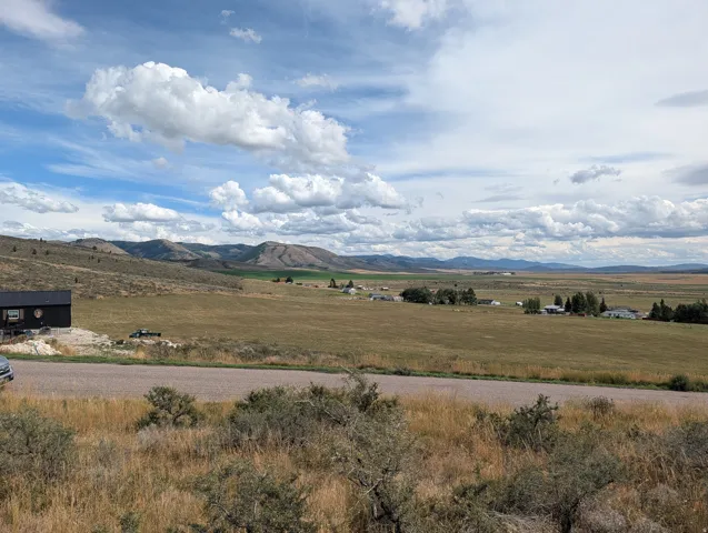 Expansive landscape featuring distant mountains, open fields, and a paved road