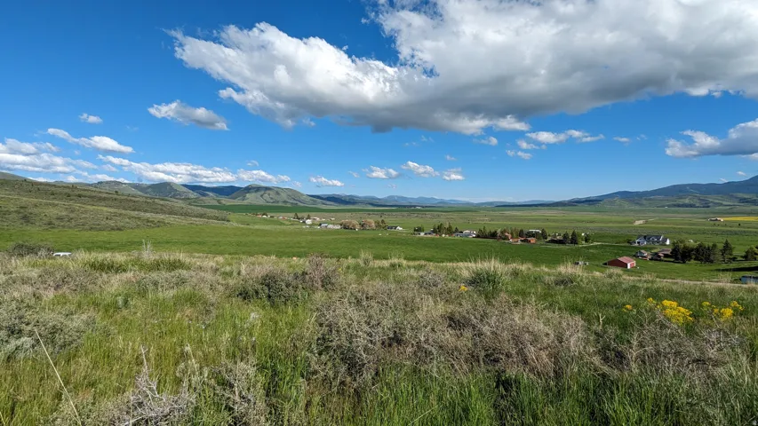 Expansive green landscape with distant rolling hills and scattered residential structures