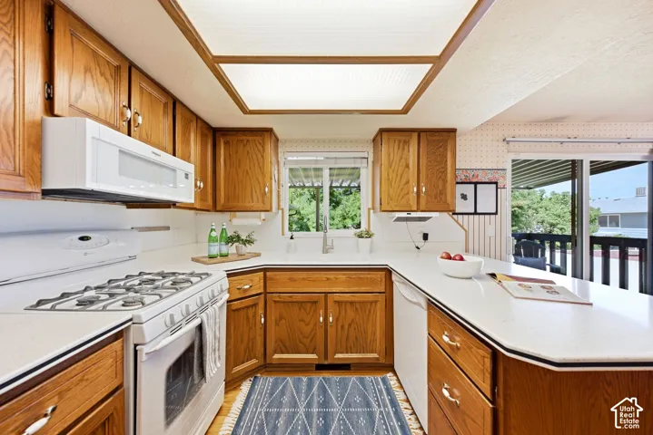 Kitchen featuring wood cabinetry, white countertops, built-in microwave, gas range, and sliding glass door to the back deck and yard access.