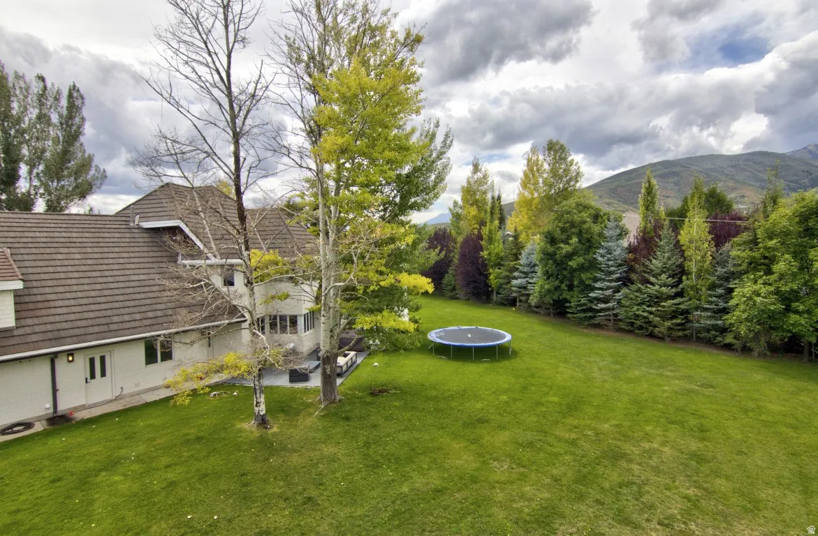Expansive green lawn, mature trees, mountain backdrop, multi-story structure with a brown tile roof, and a visible patio area
