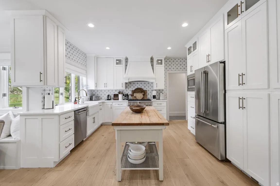 Bright kitchen featuring extensive white cabinetry, stainless steel appliances, a center island with a wood-finish countertop, and wood-finish flooring