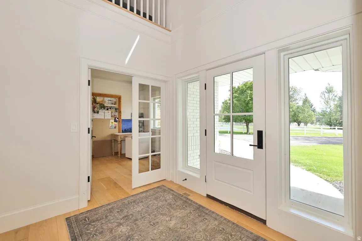 Light wood-finish flooring, white paneled entry door with glass, sidelight windows, and transom windows